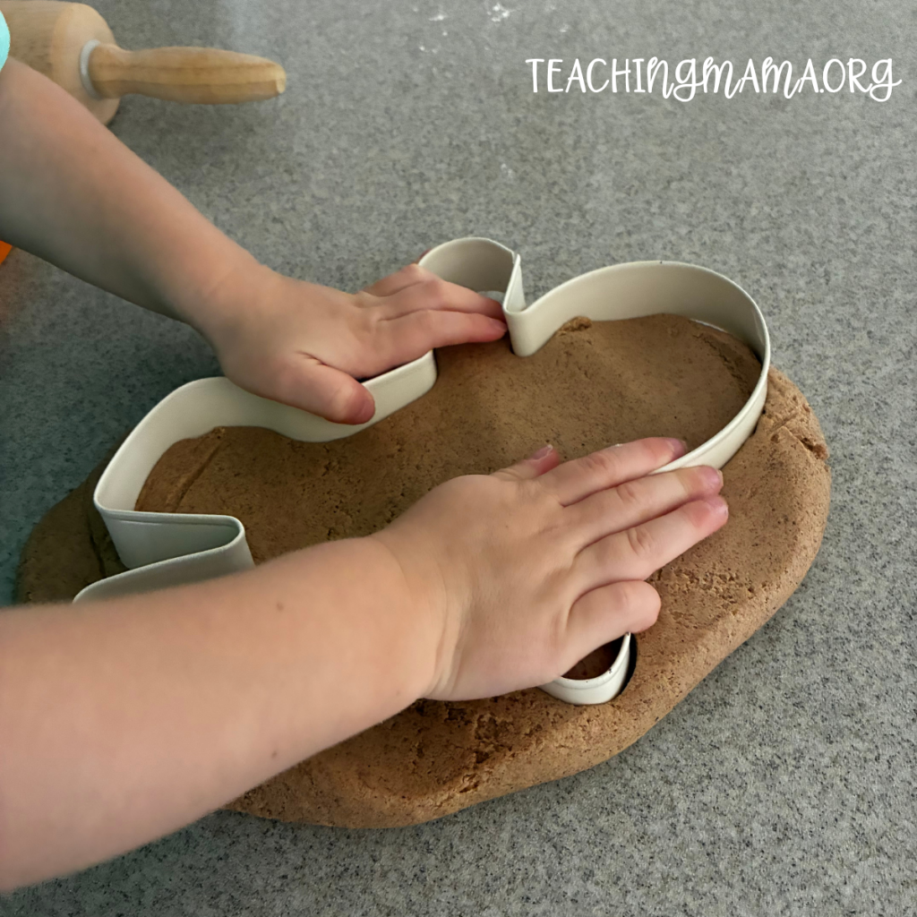 child using gingerbread man cookie cutter on playdough